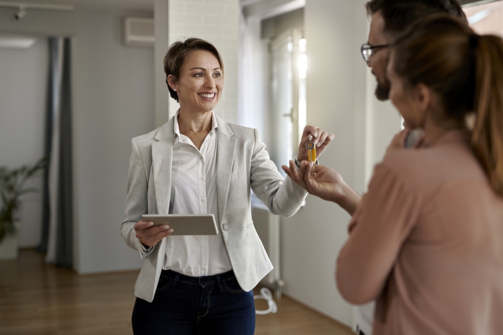 Happy real estate agent giving to a couple keys of their new home.