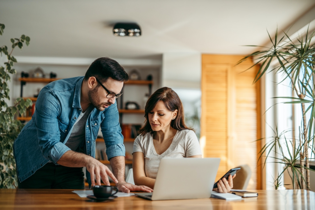 Two people discussing paperwork and working on a laptop, portrait.